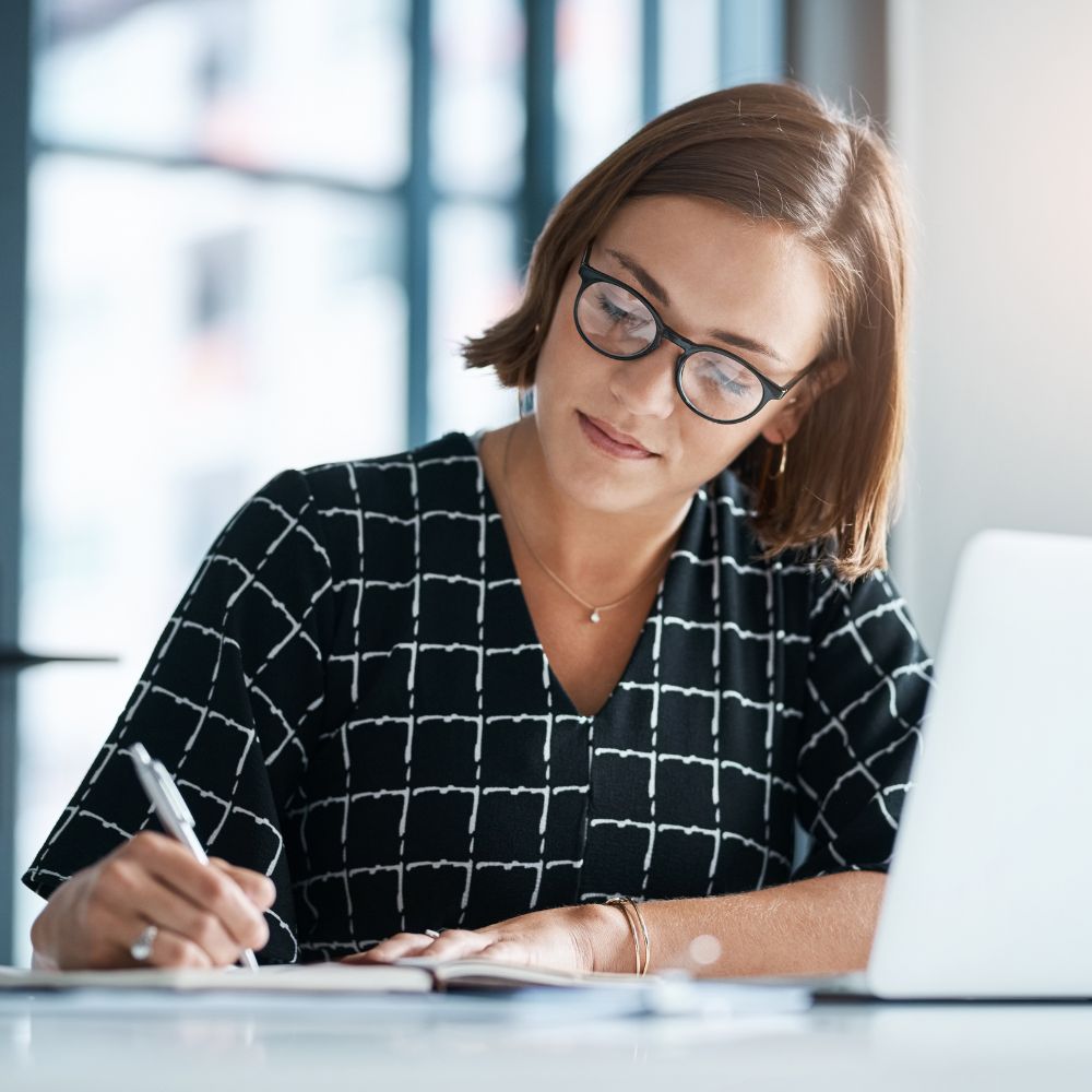 A woman writing a grant with a computer in front of her.