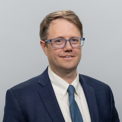 Male in blue suit and glasses against gray background