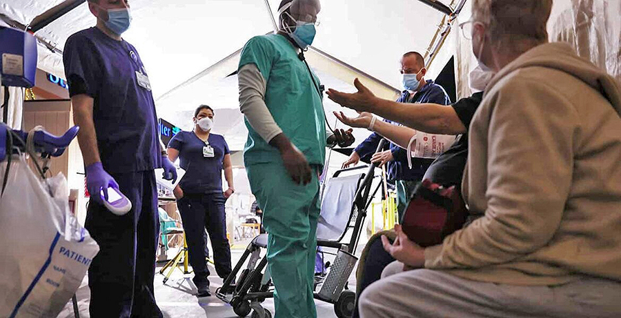 Clinicians evaluate incoming patients with their arms raised in a triage tent set up in the parking lot at Providence St. Mary Medical Center