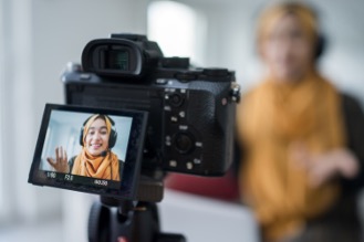Video camera display showing a woman wearing an orange hijab recording video content.