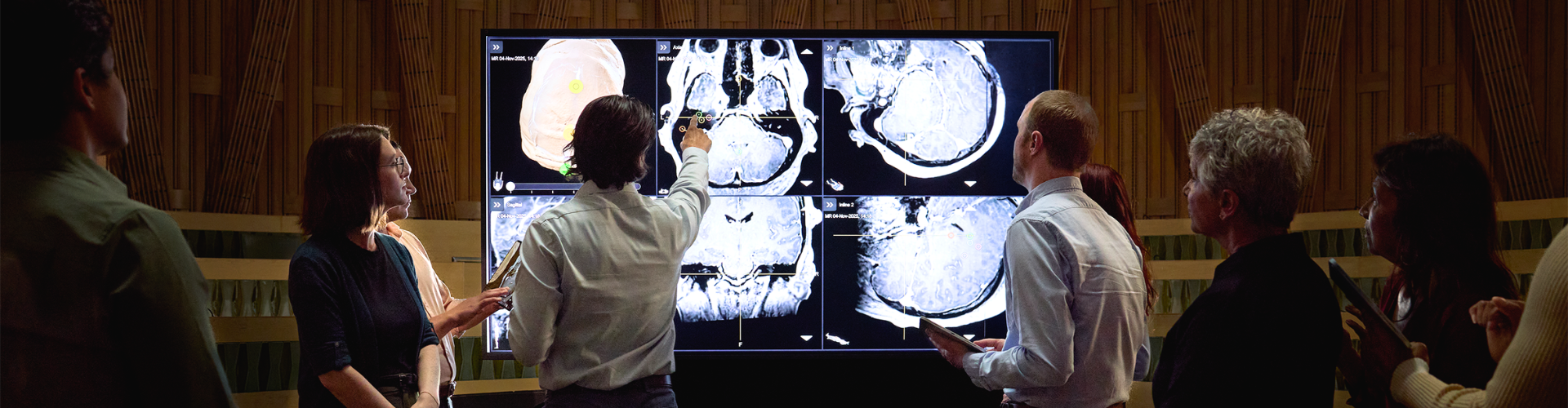 a group of doctors looking on as a male doctor points to a screen filled with different brain scans