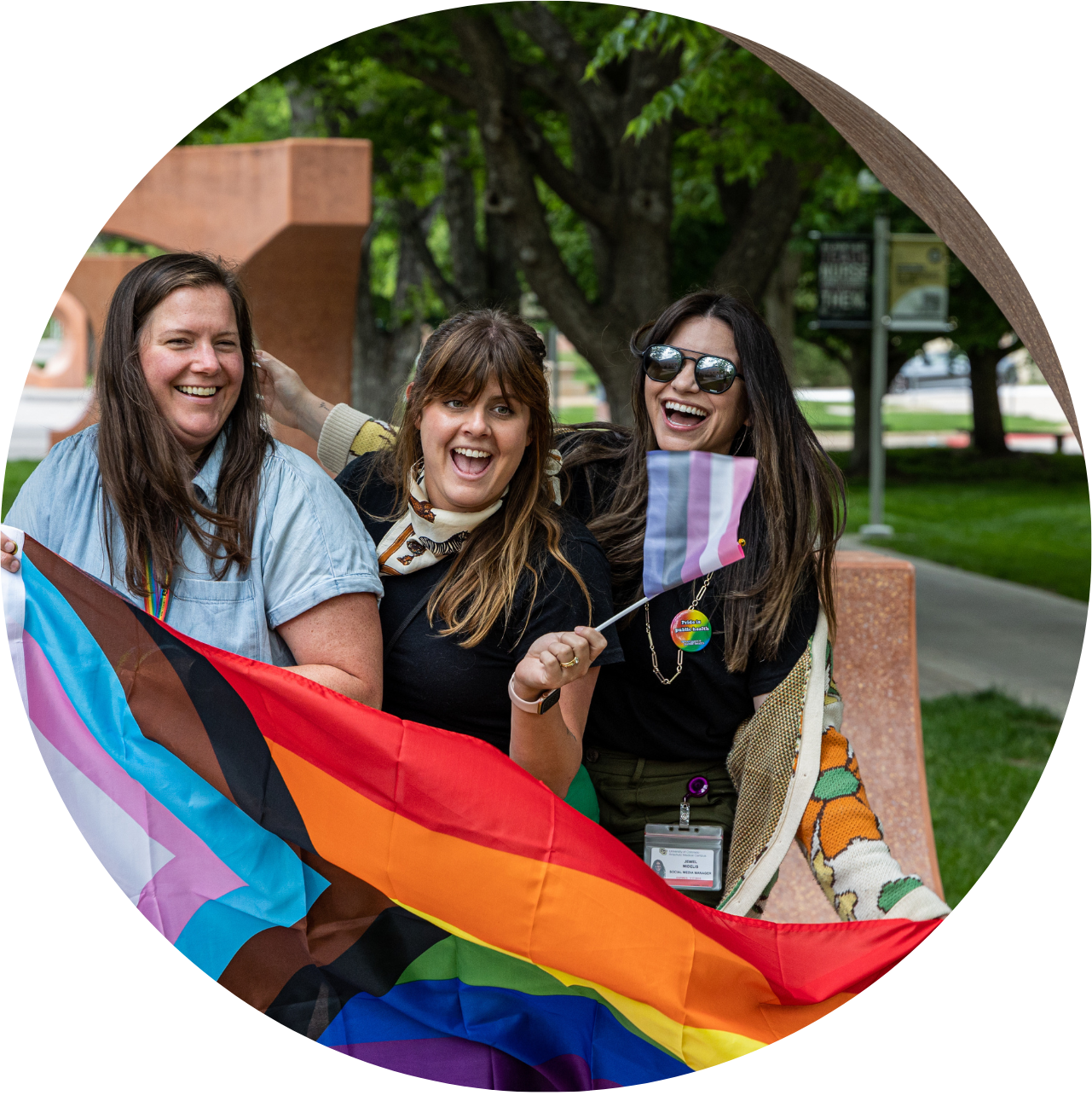 Three women smiling while holding a pride flag