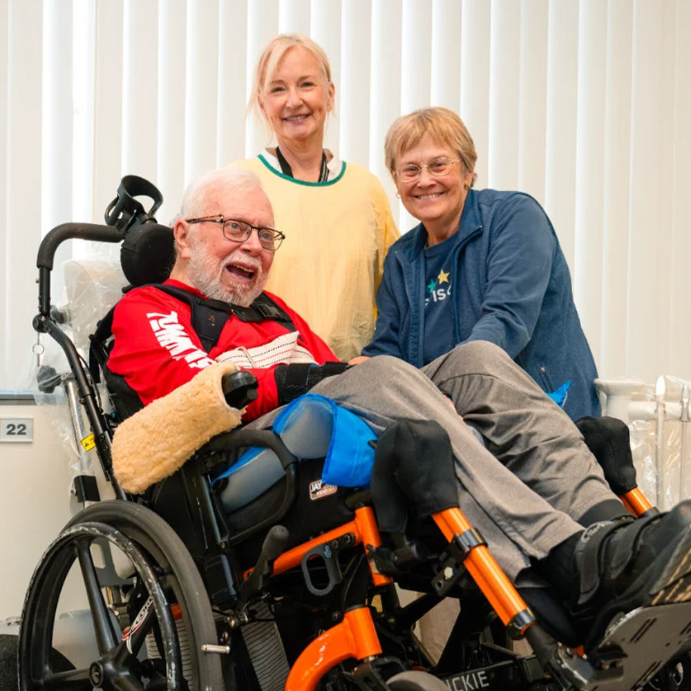 Two women nurses standing with a man in a wheelchair smiling