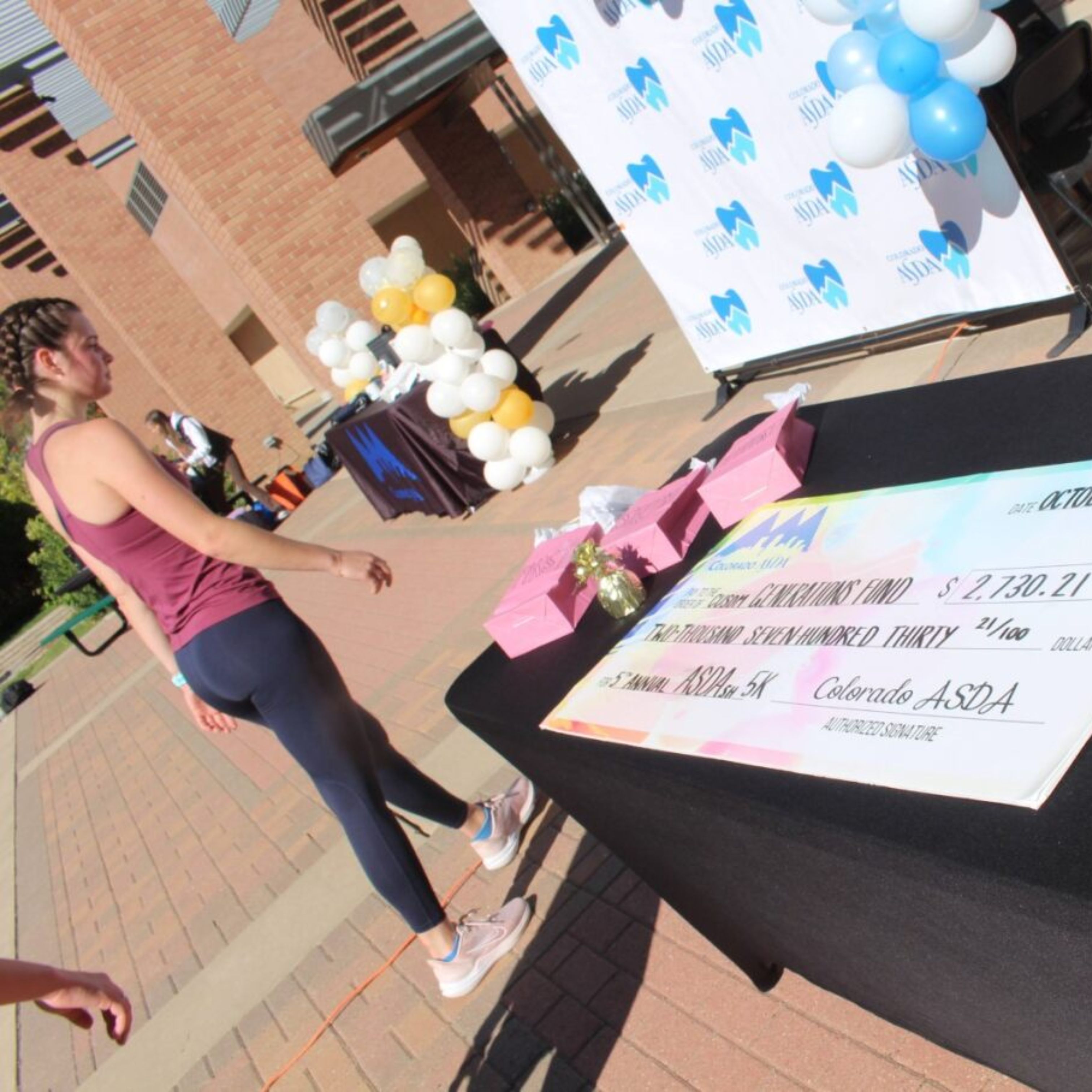 Student walks by a giant check laid out on a table, showing an amount of $2,730.21 from Colorado ASDA.