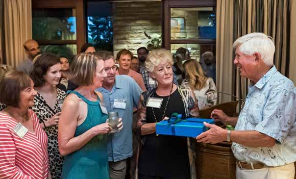Dr. Schorr hands a gift wrapped in blue packaging over to colleagues.