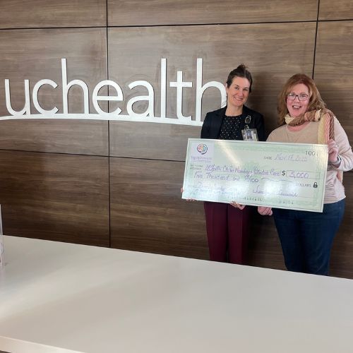 Jenni holds up a giant check for $5,000 in front of a UCHealth sign.