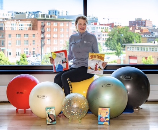 Joanne Myer surrounded by fit balls, poses with books and videos demonstrating their use.