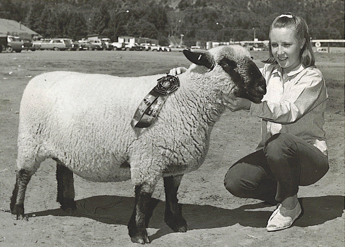 Karen Zink as a child, kneeling next to a sheep that is sporting a prize ribbon.