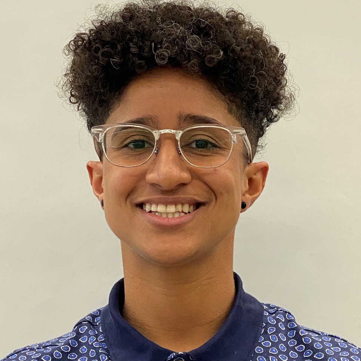 Tori Serna, physical therapy scholar. Tori is smiling at the camera and wearing glasses and a blue patterned shirt.