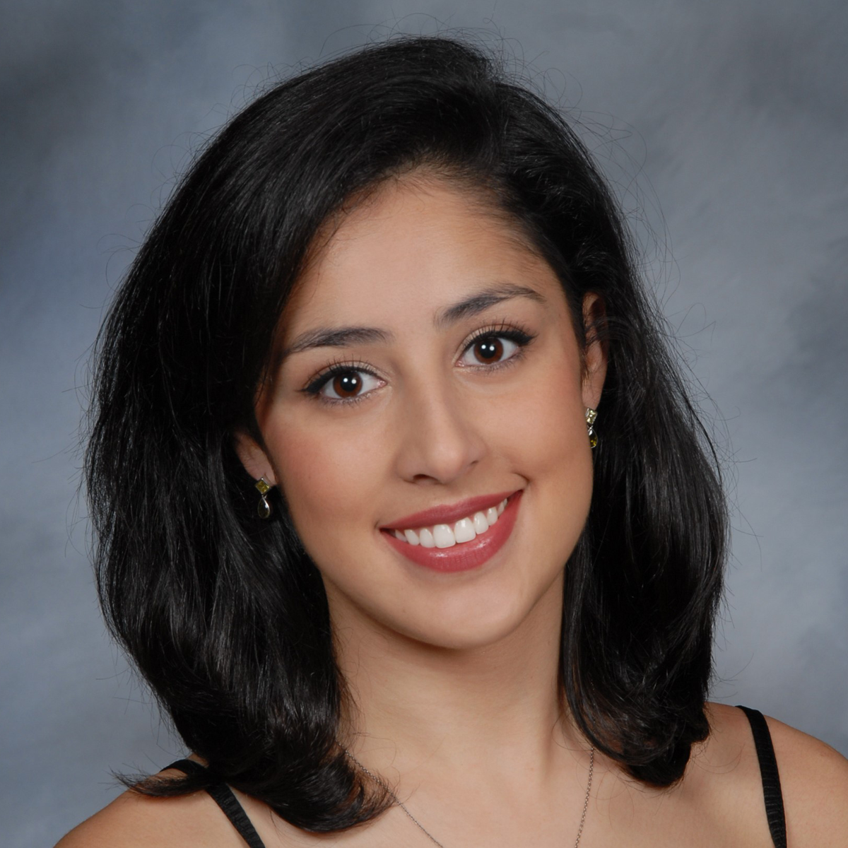 Camila Vargas, medical scholar. She is smiling at the camera and is against a light gray photography studio background.