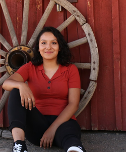 Photo of Erika sitting against a wagon wheel propped on red barn door.