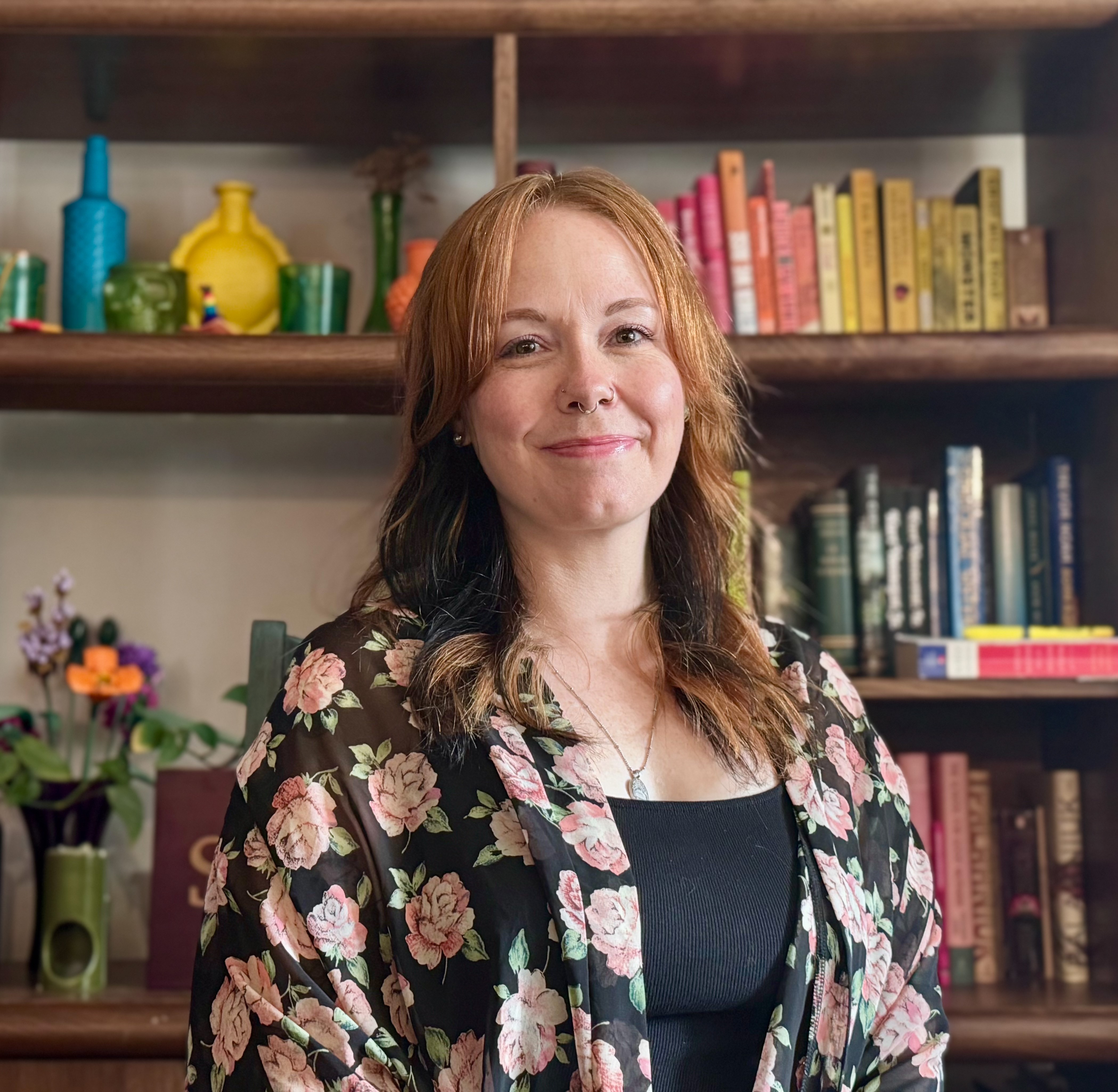 Tessa Carlson, smiling, in front of a bookshelf with books, flowers, and vases