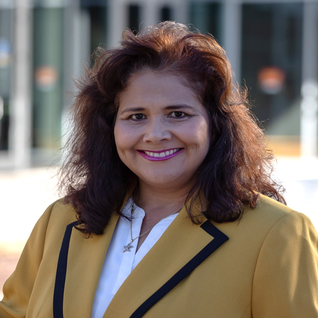 Professional headshot of Adela Cota-Gomez, she smiles wearing a yellow blazer in an outdoor setting.