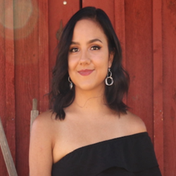 Professional Photo of Karely Villareal Hernandez; she smiles and wears a black top in front of a red wooden door