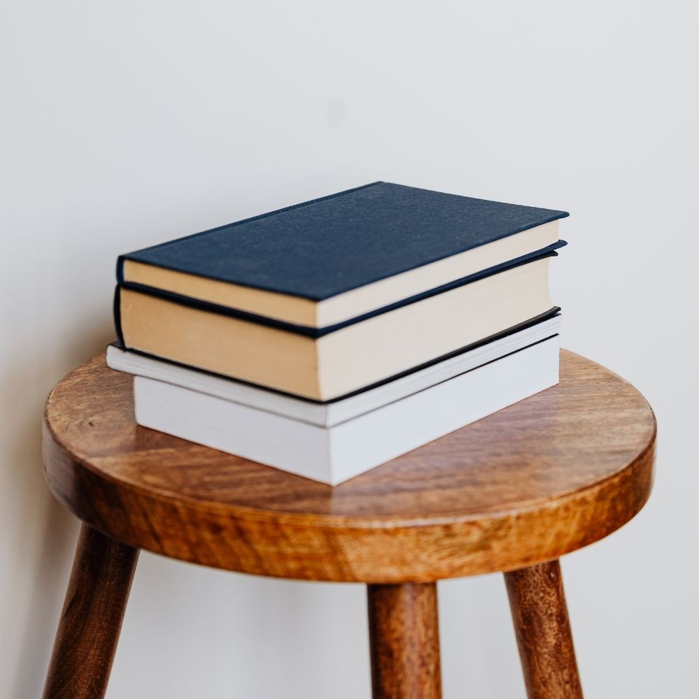 A stack of books sitting on a stool.