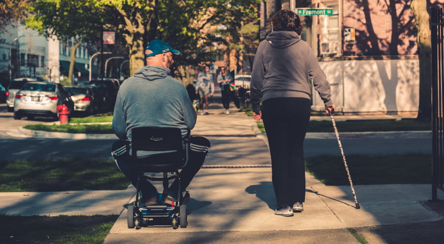man in wheelchair and blind woman walking down street