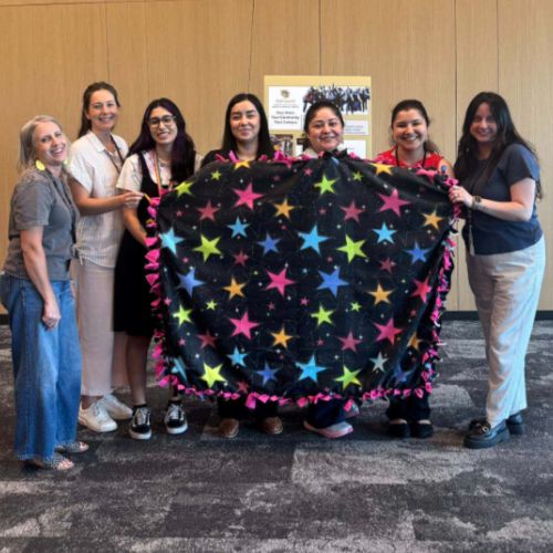 A team of CU Anschutz Staff members hold up a completed blanket printed with stars.